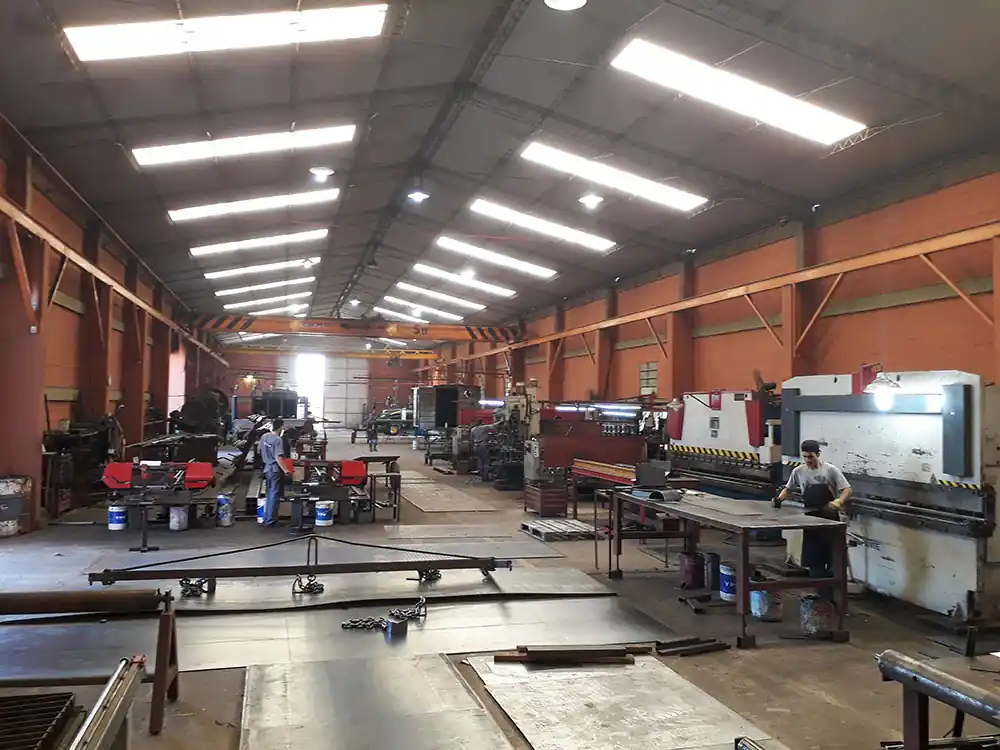 Interior de la nave de producción de ACEPLA, con operarios trabajando entre plegadoras y mesas de armado